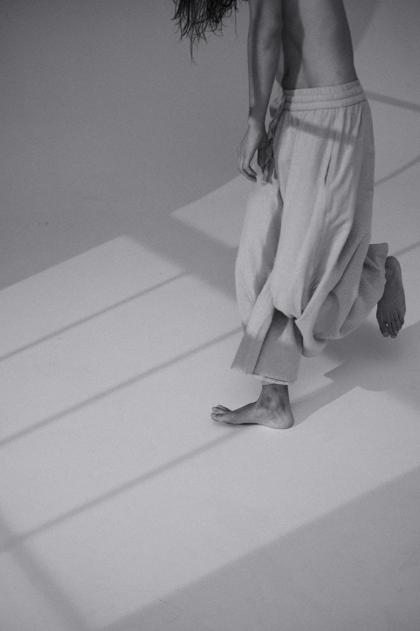 Black and white photo of a model’s legs and trousers in a pattern of window light