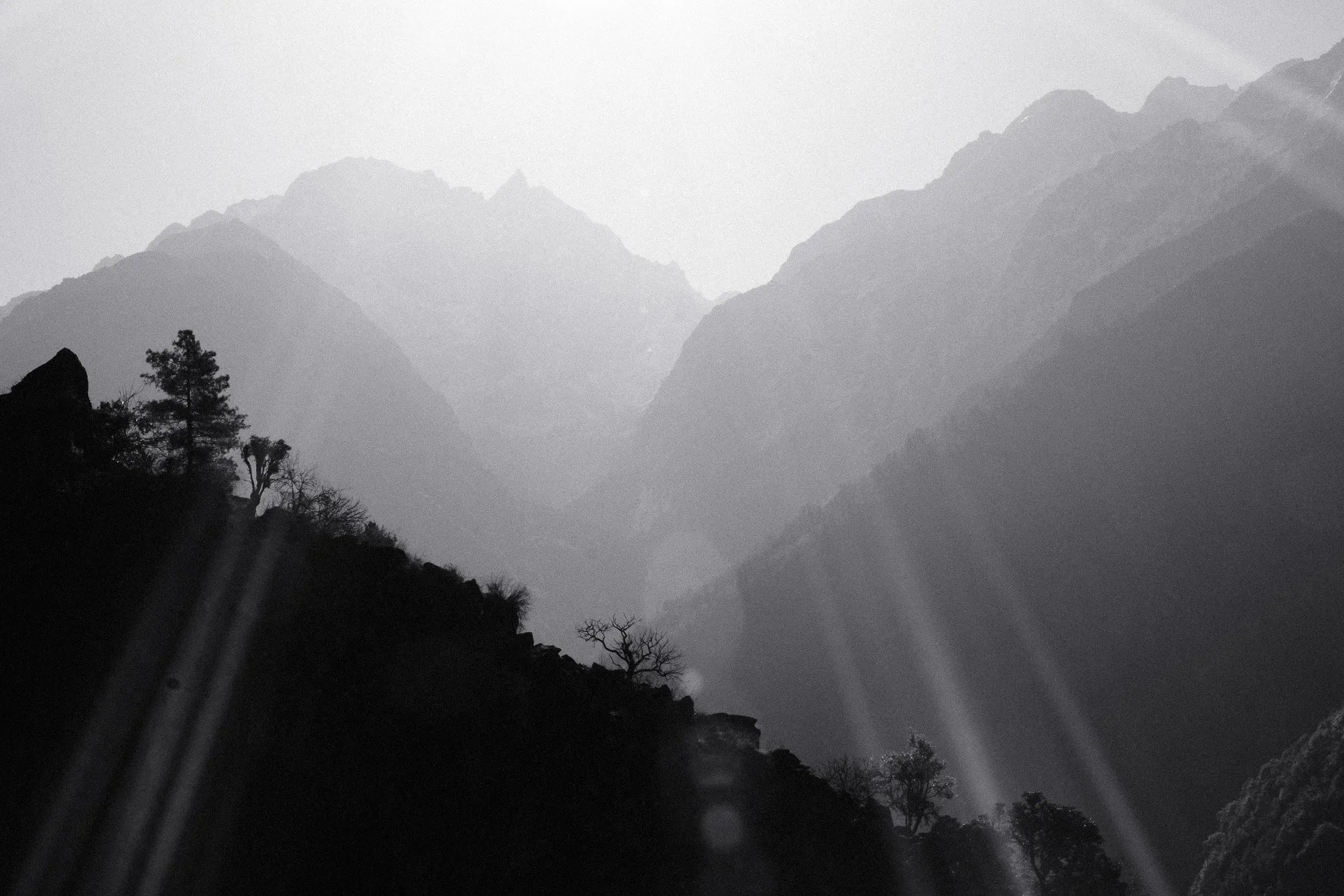 Black and white photo of sun rays over layered mountain ridges in silhouette