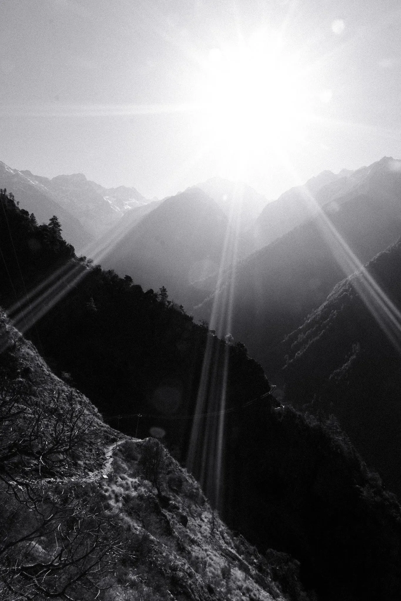 Black and white photo of the sun bursting over a mountainside above the trail