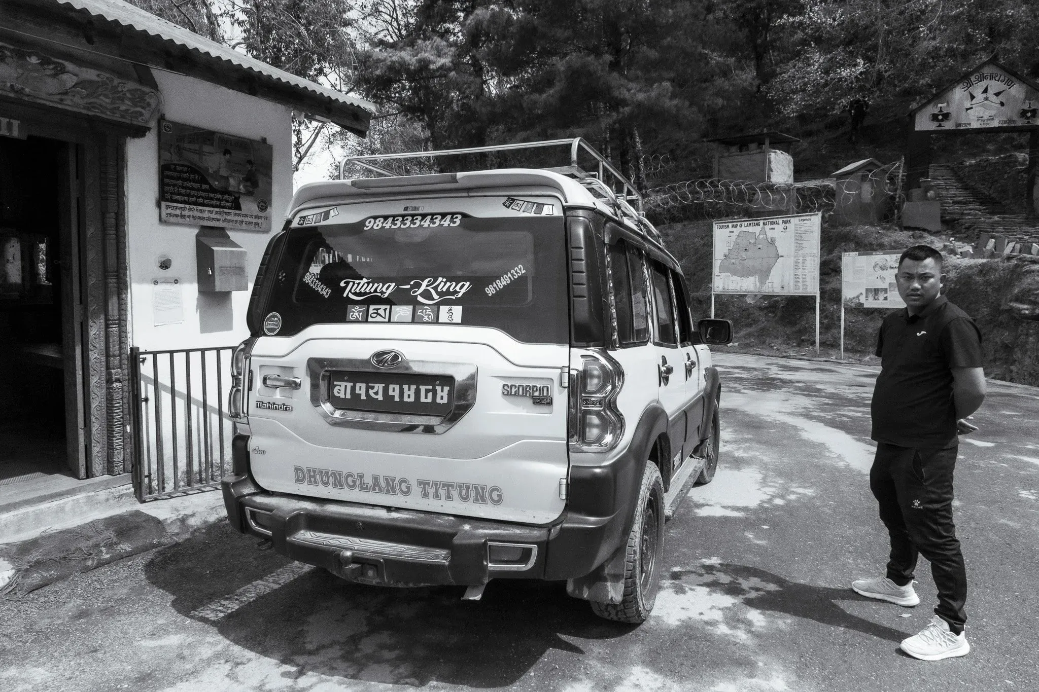 Black and white photo of a man standing beside a jeep in Syabrubesi