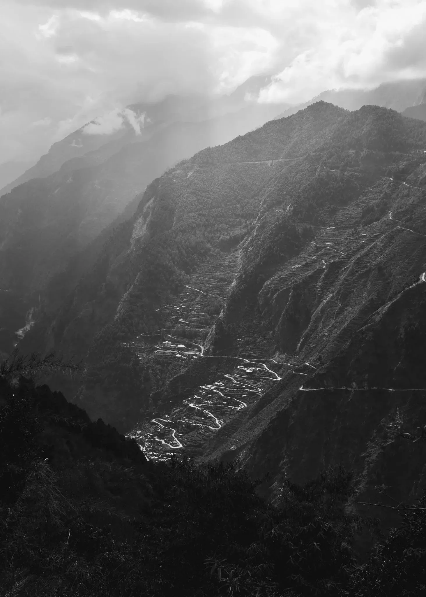 Black and white photo of terraced fields on a steep mountainside under cloud