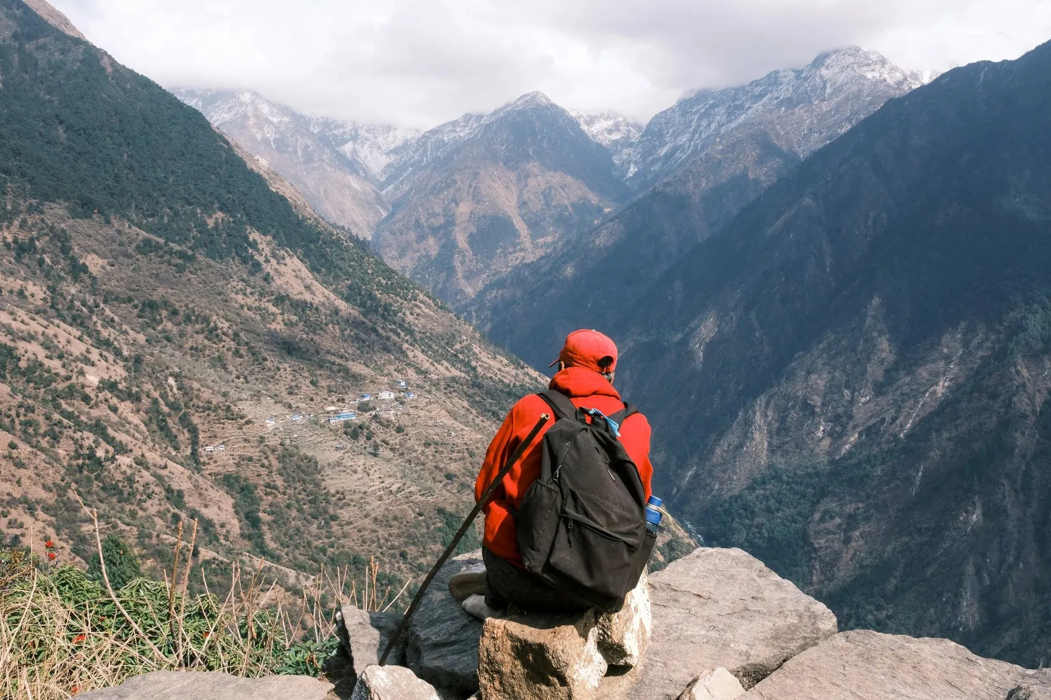 A trekker in a red jacket sits on a rock looking down the Langtang valley