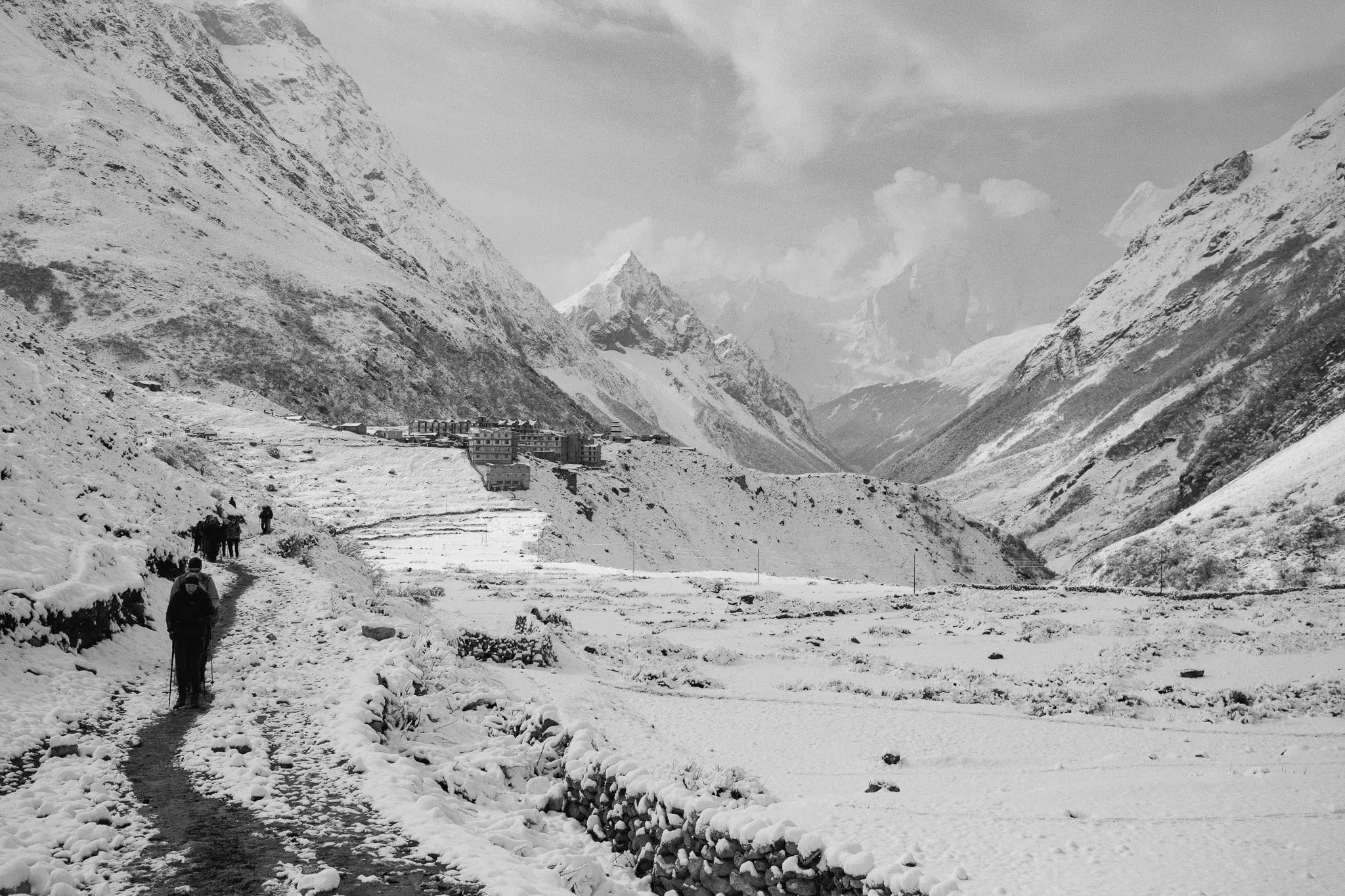 Black and white photo of trekkers on a snowy trail through a wide valley towards Dharamsala