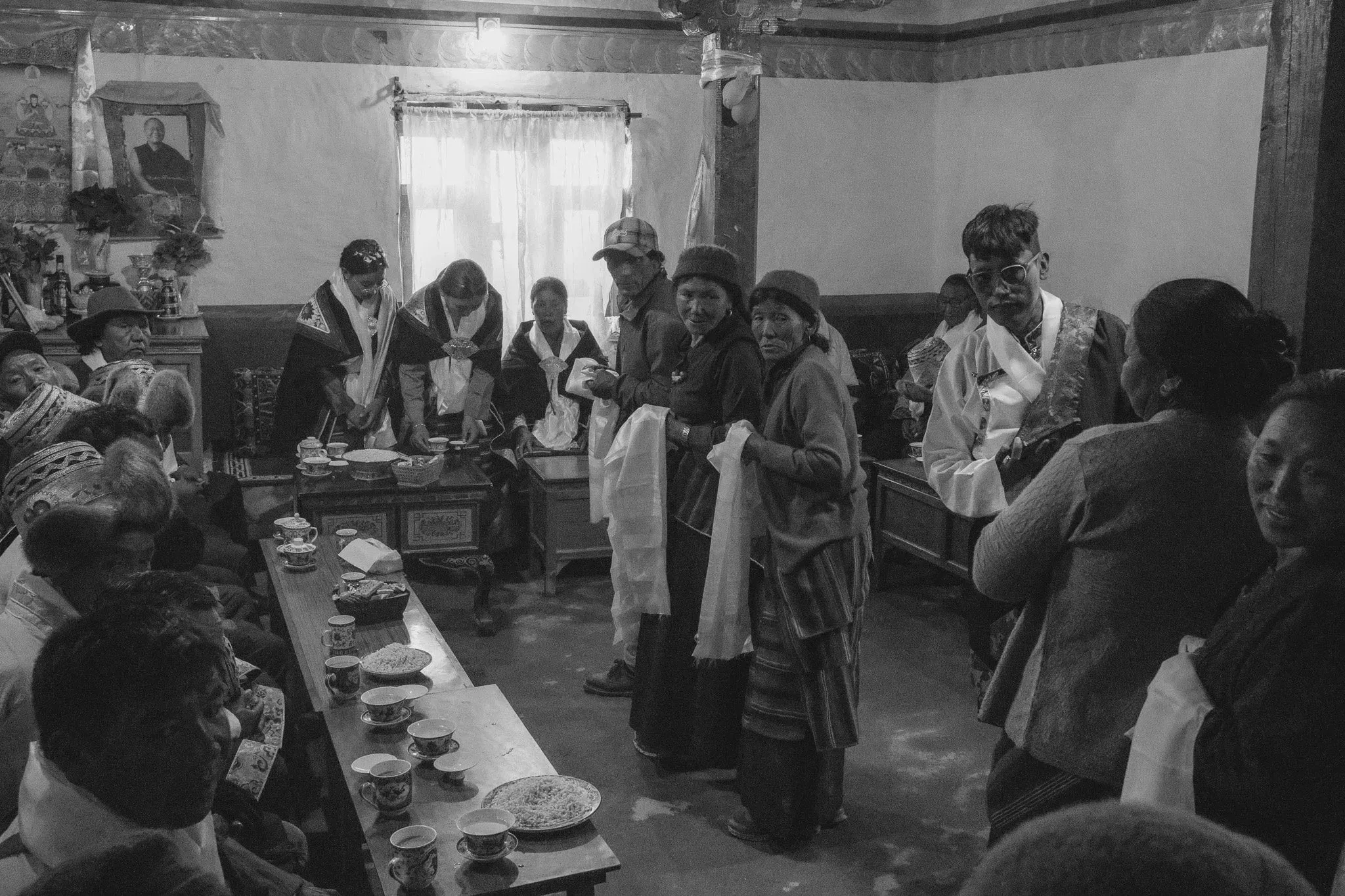 Black and white photograph of villagers gathered around a table at a celebration near Tsarang, Upper Mustang, Nepal.