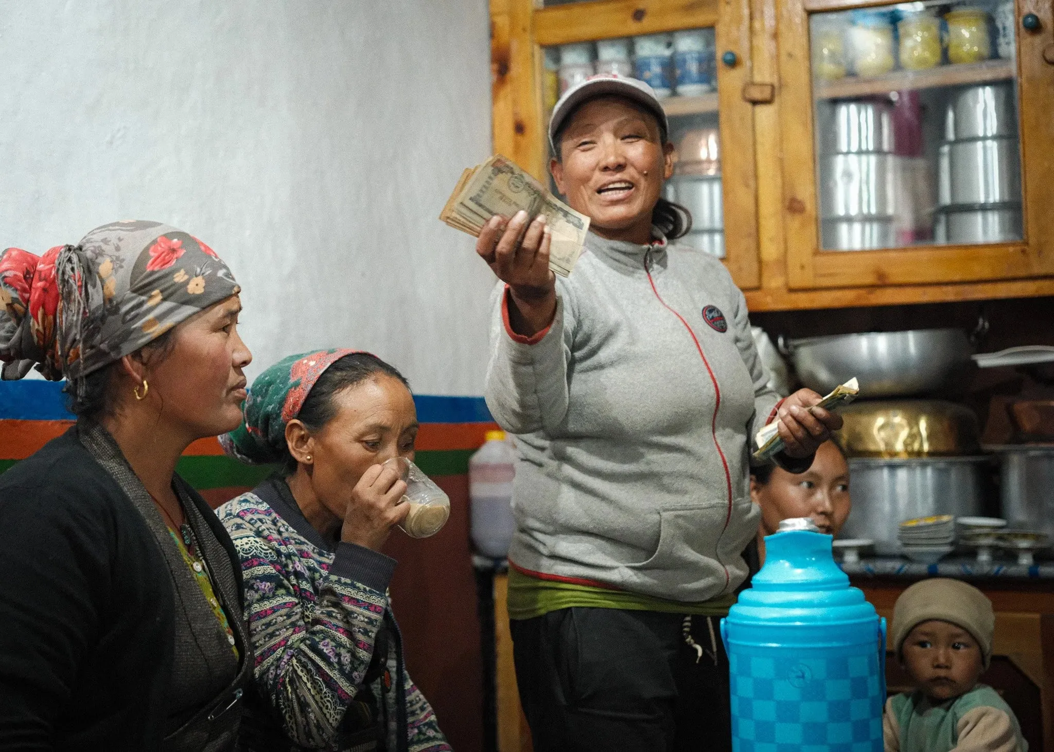 Women sharing tea in a kitchen in Tsarang, one holding out money