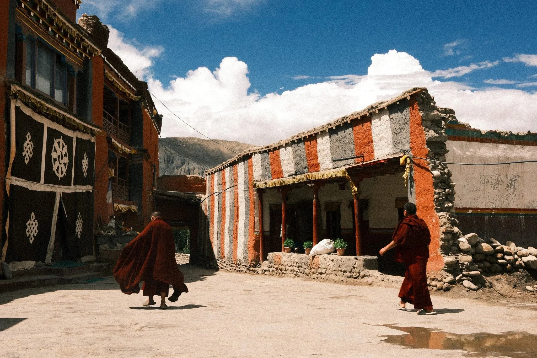 Monks in maroon robes crossing a courtyard in front of the monastery in Tsarang