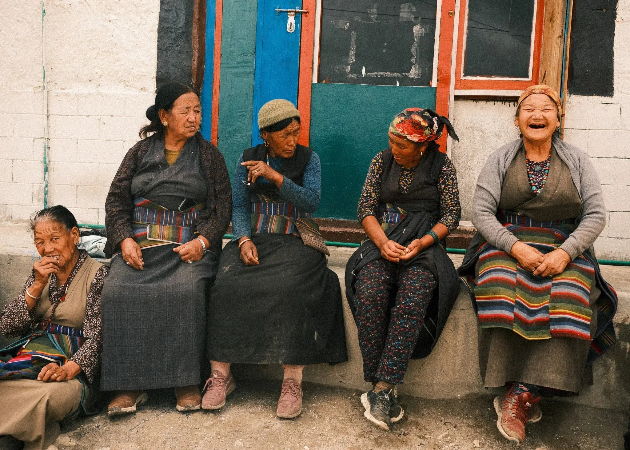 Older women in striped aprons laughing together on a bench in Tsarang