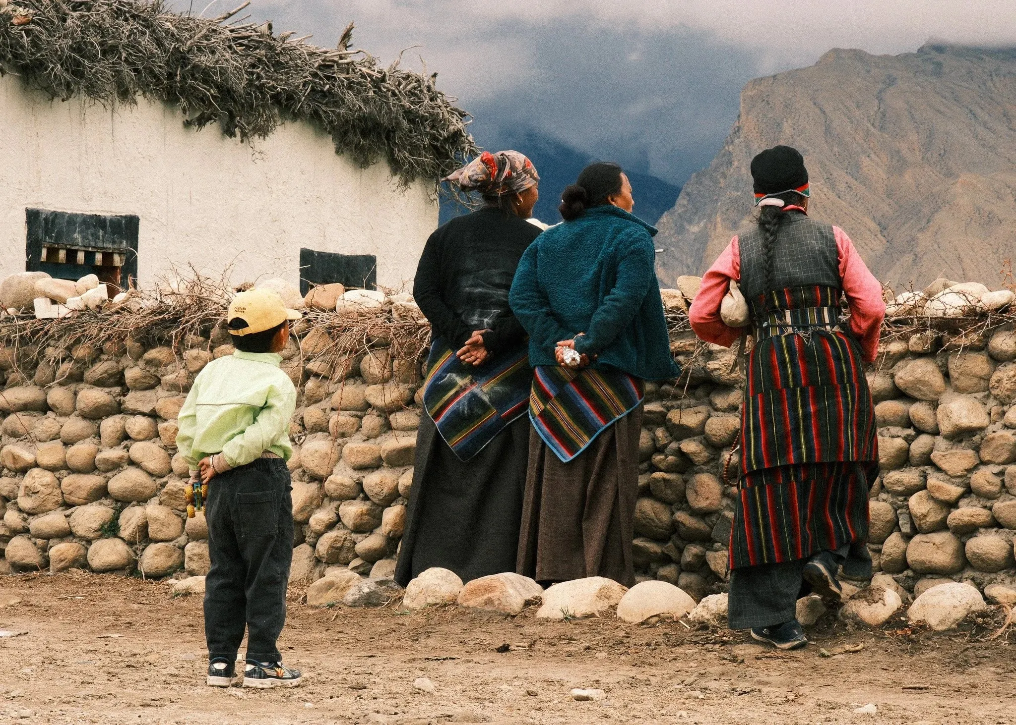 Women and a child standing by a stone wall looking towards the mountains in Tsarang