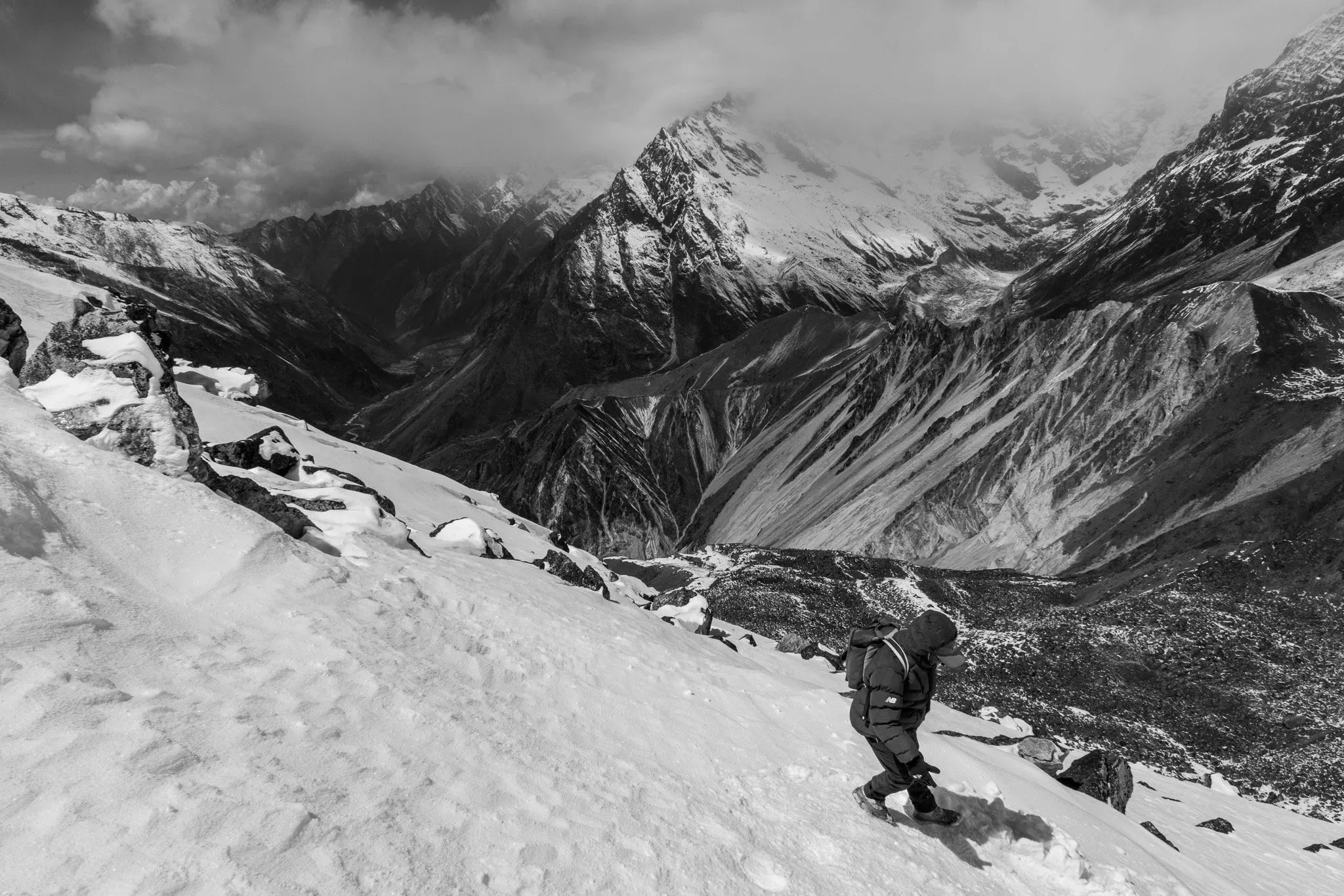 Black and white photo of a trekker climbing a snowy slope below the peaks