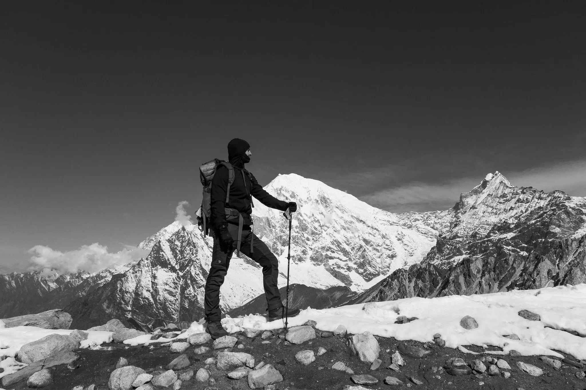 Black and white photo of a trekker with poles standing in front of snow-covered peaks on Tserko Ri