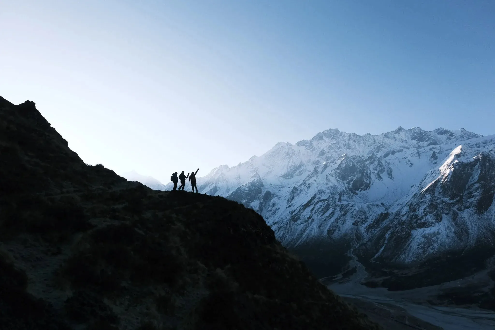 Three trekkers in silhouette on a ridge with snow-covered Langtang peaks behind