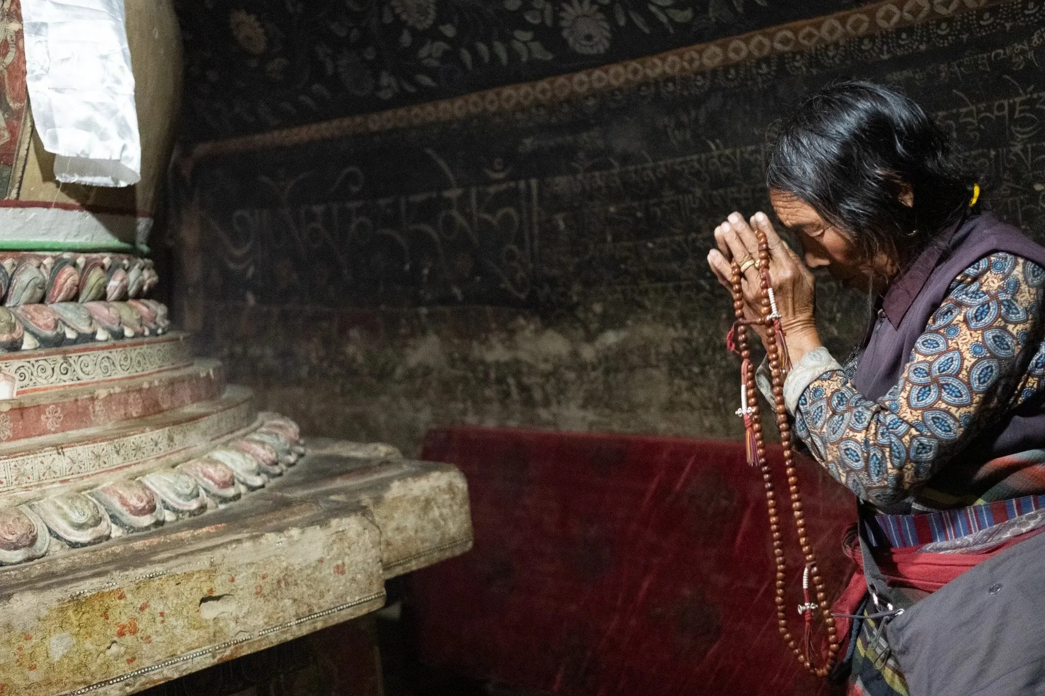 Woman holding prayer beads beside a painted stupa inside a monastery near Luri Gompa, Upper Mustang, Nepal.