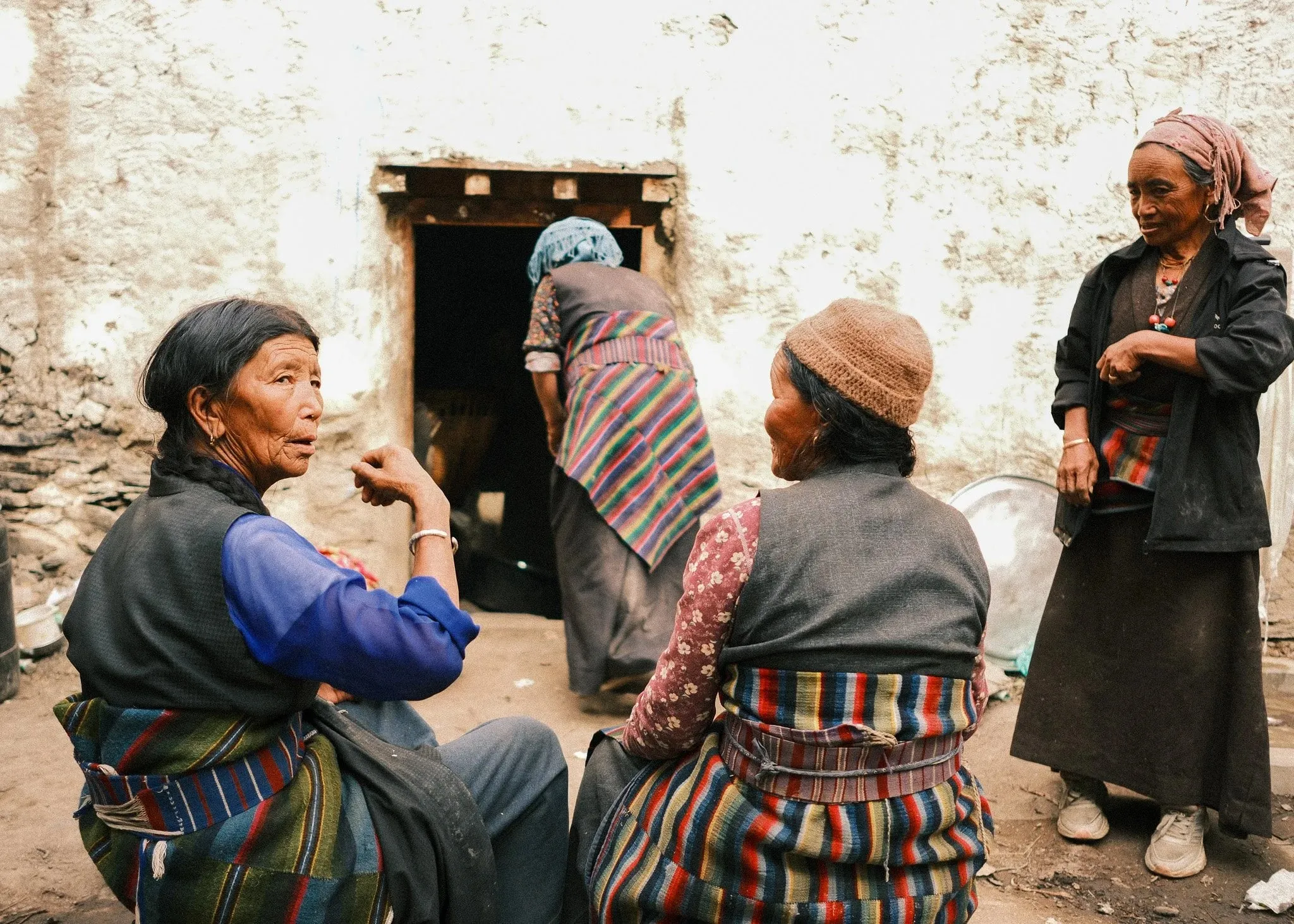 Women gathering outside a whitewashed doorway, wearing colourful striped aprons in Dhakmar, Upper Mustang, Nepal.