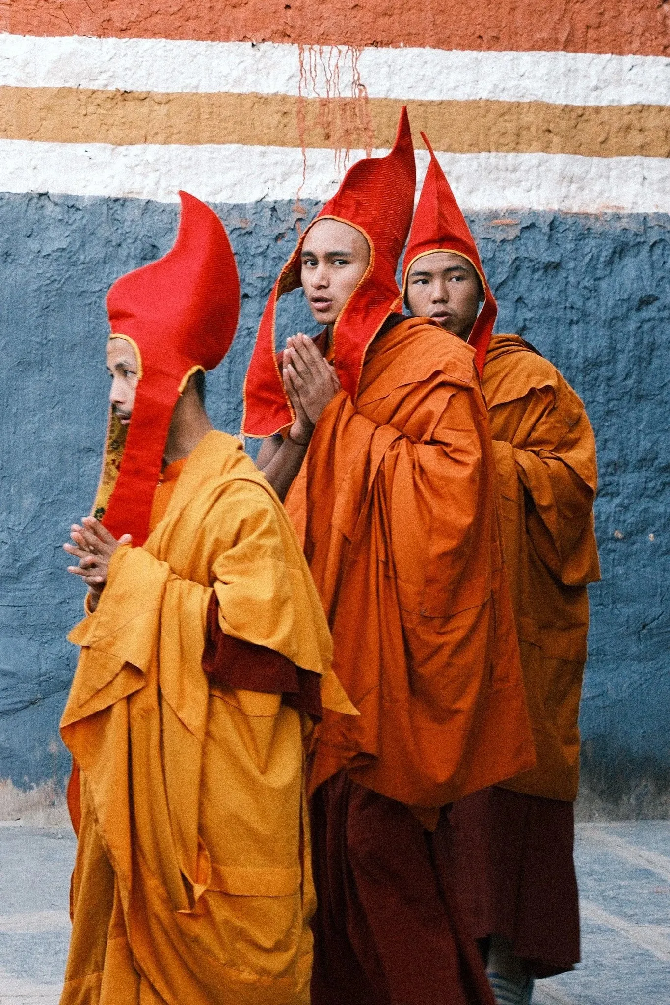 Young monks wearing orange and red robes and tall ceremonial hats in Lo Manthang, Upper Mustang, Nepal.
